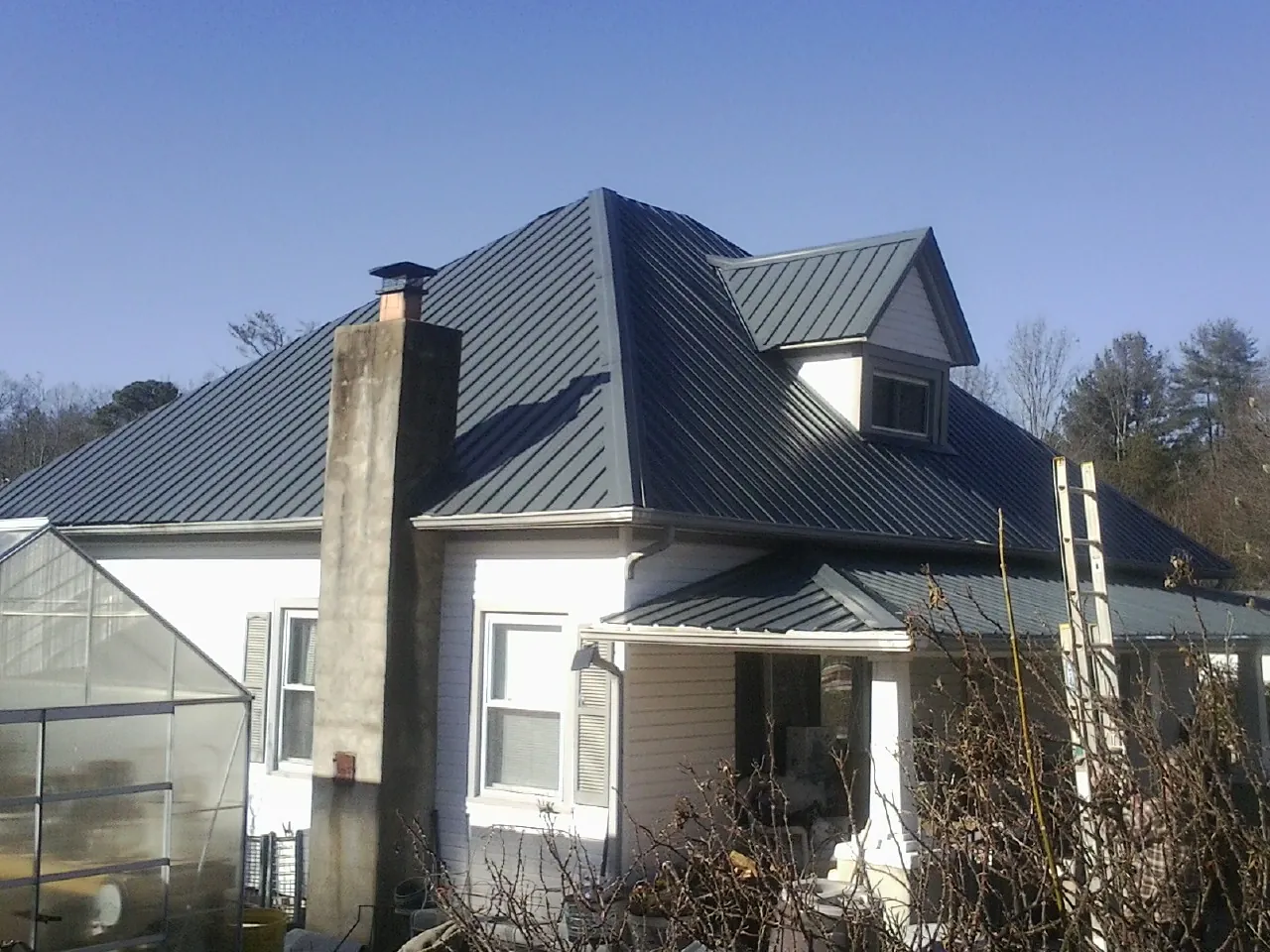 Dark blue standing seam metal roof on a white farmhouse with dormer — Slate & Tile Roof Repair by Roofing Brothers in Saginaw
