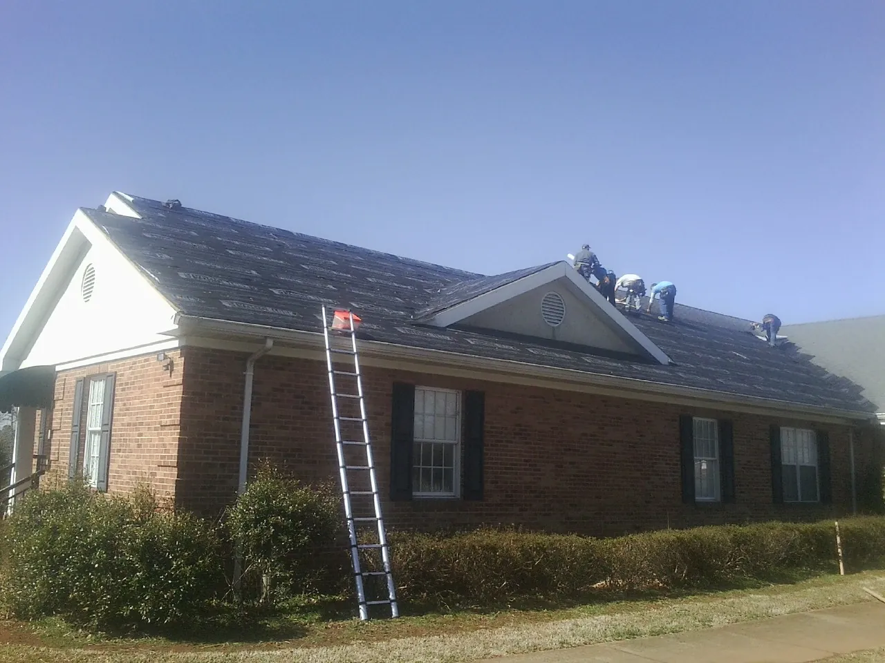 Crew tearing shingles off a brick ranch roof with a ladder set — Metal Roof Repair work by our crew in Saginaw