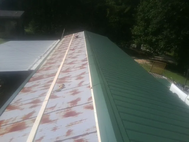 Old rusted panels beside newly installed green metal roofing — Wind Damage Roof Repair by Roofing Brothers in Saginaw