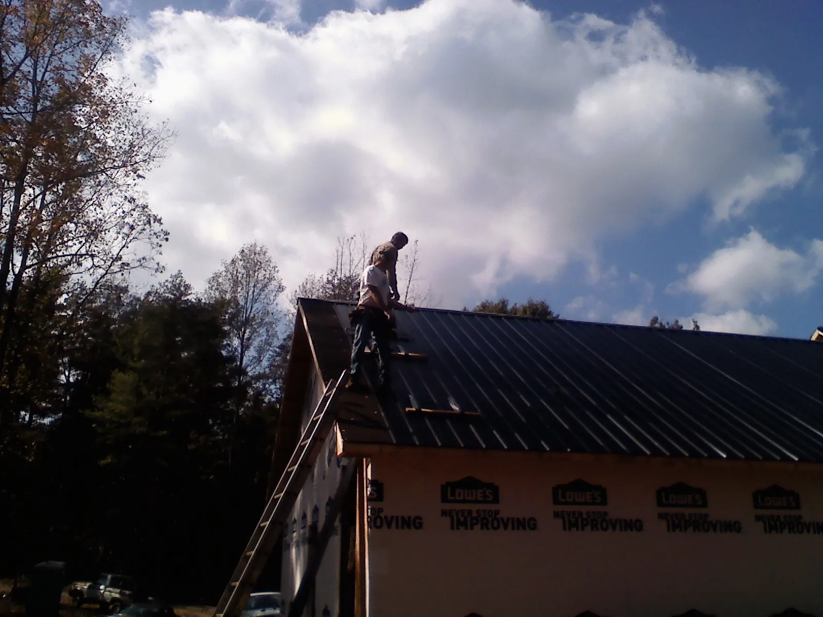 Roofer fastening dark metal panels high against a cloudy sky, from a Roof Inspection job in Saginaw
