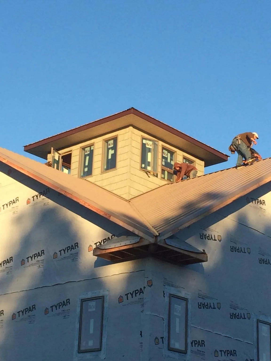 Roofers working around a rooftop cupola on a new metal roof at sunset — Roof Waterproofing in Saginaw by Roofing Brothers